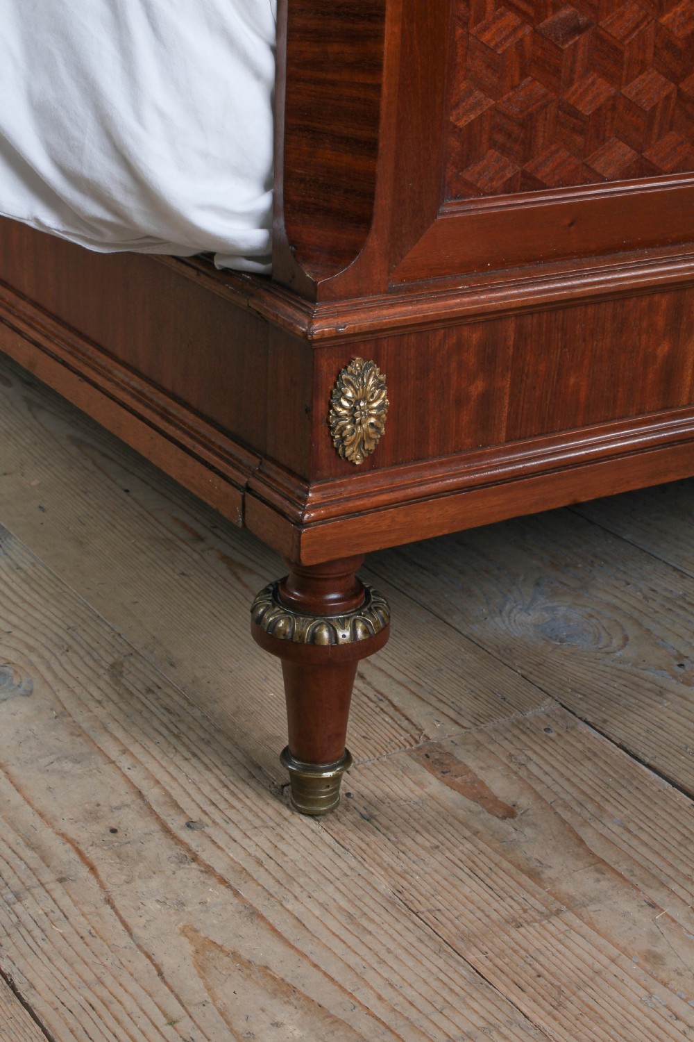 An antique French mahogany bed frame featuring geometric parquetry panels, fruitwood ribbon marquetry on the footboard, and gilt bronze mounts. View IV
