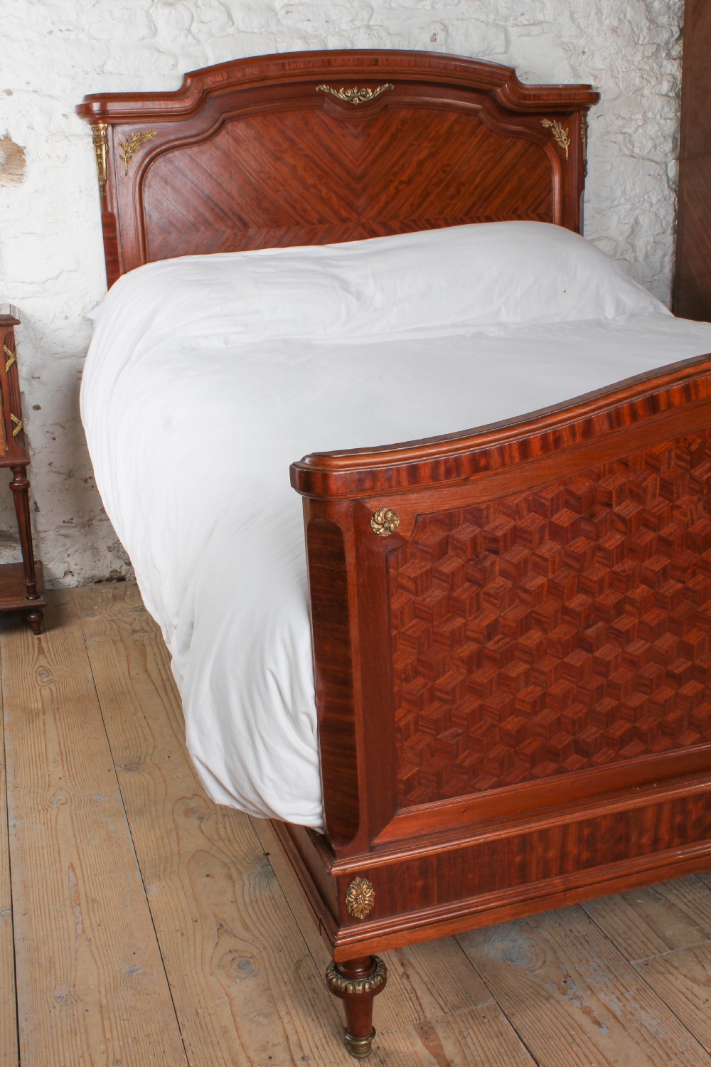 An antique French mahogany bed frame featuring geometric parquetry panels, fruitwood ribbon marquetry on the footboard, and gilt bronze mounts. View IX