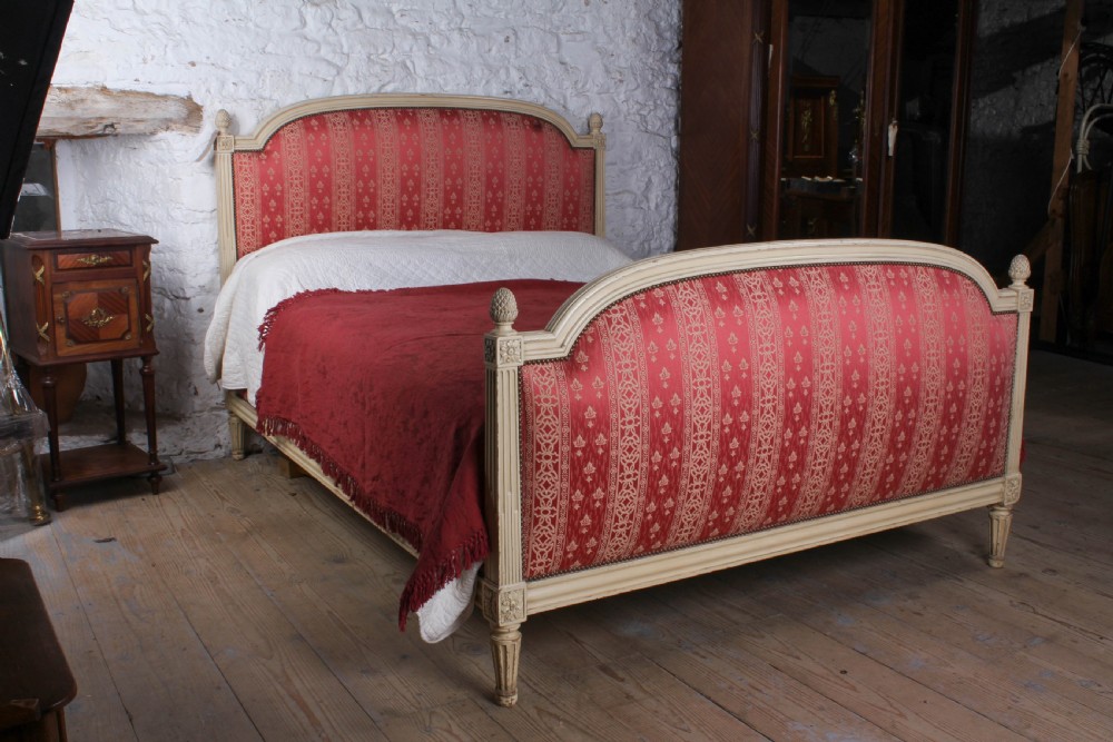 A French Louis XVI style king size bedstead featuring a cream painted carved timber frame and red patterned damask upholstered headboard and footboard.
