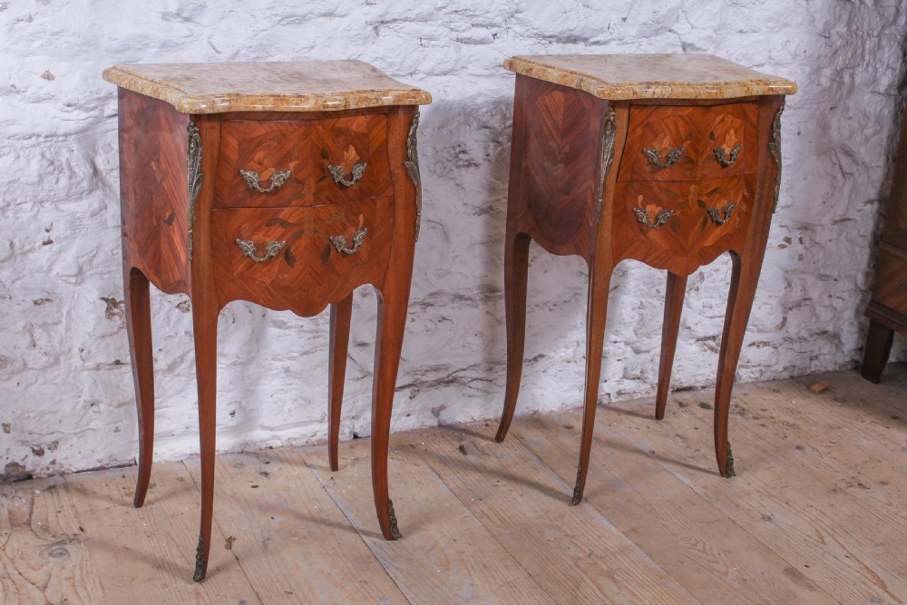 A pair of French Louis XV style bow-front bedside tables featuring floral marquetry inlay, cabriole legs, brass handles, and marble tops.