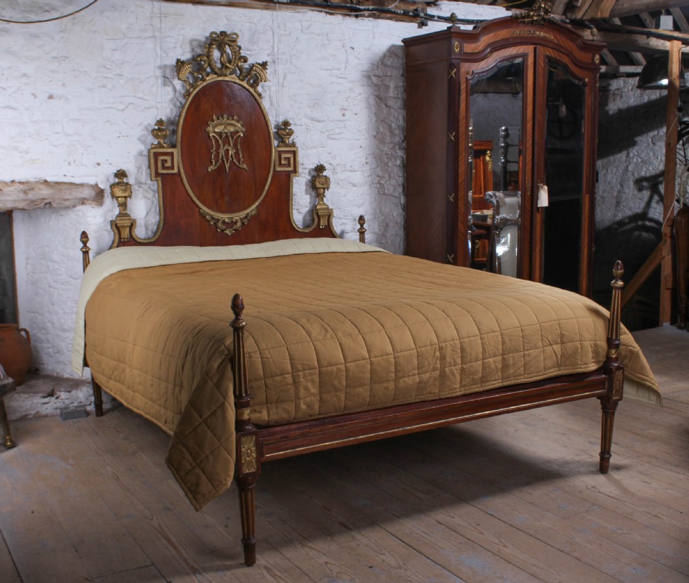 An antique mahogany super king bed featuring a high headboard with an oval central medallion, carved giltwood crest, Greek key motifs, and turned posts.