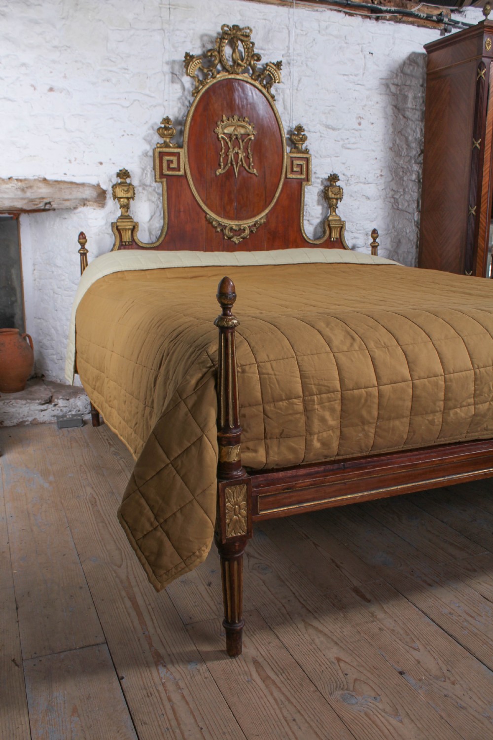 An antique mahogany super king bed featuring a high headboard with an oval central medallion, carved giltwood crest, Greek key motifs, and turned posts. View III