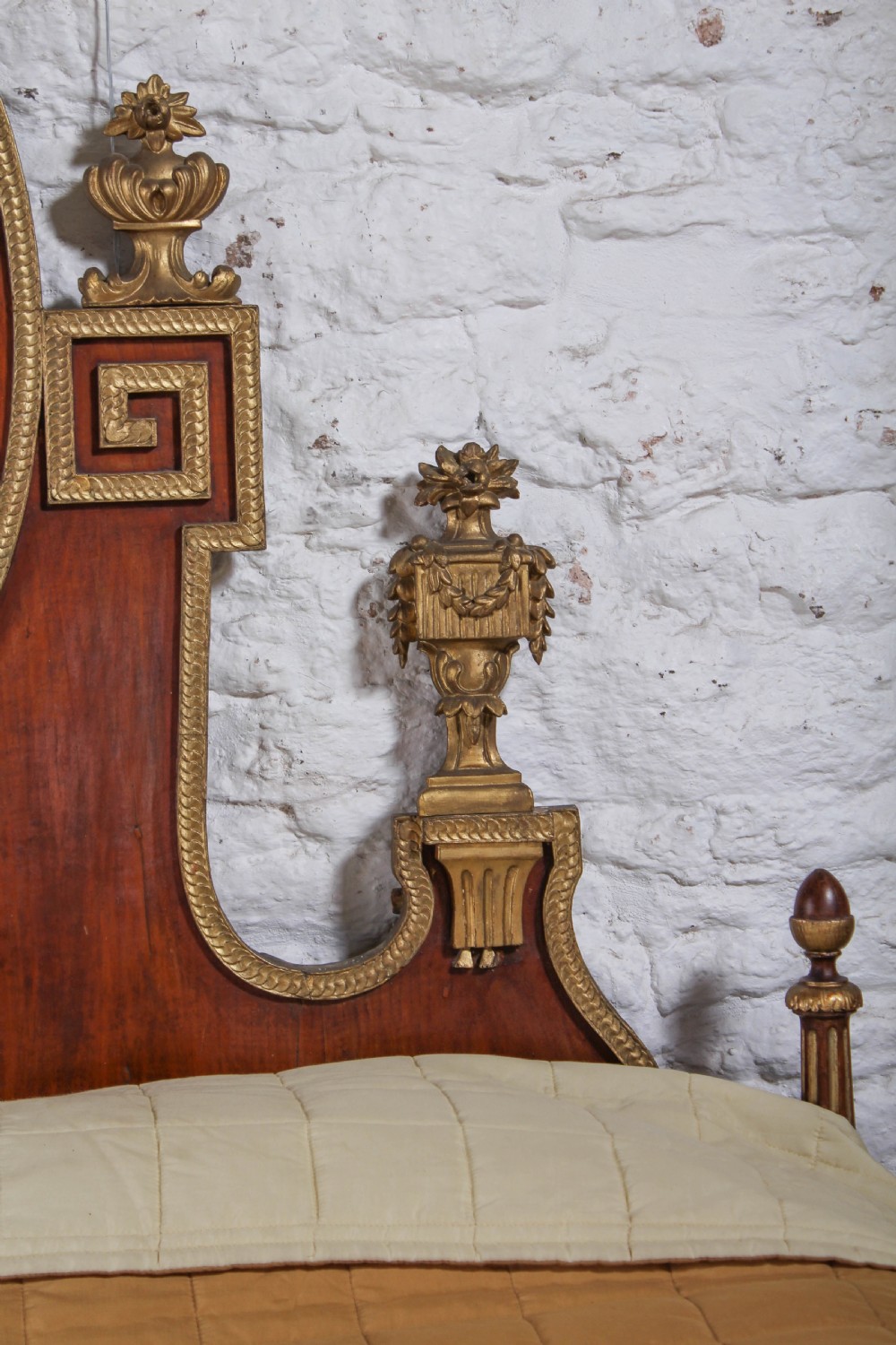 An antique mahogany super king bed featuring a high headboard with an oval central medallion, carved giltwood crest, Greek key motifs, and turned posts. View IV