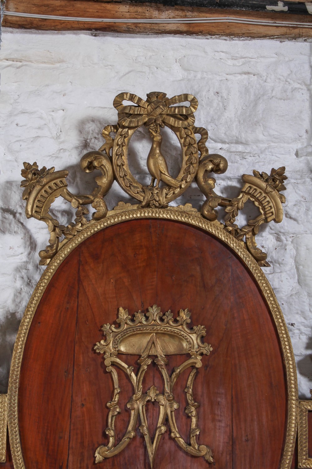 An antique mahogany super king bed featuring a high headboard with an oval central medallion, carved giltwood crest, Greek key motifs, and turned posts. View VII