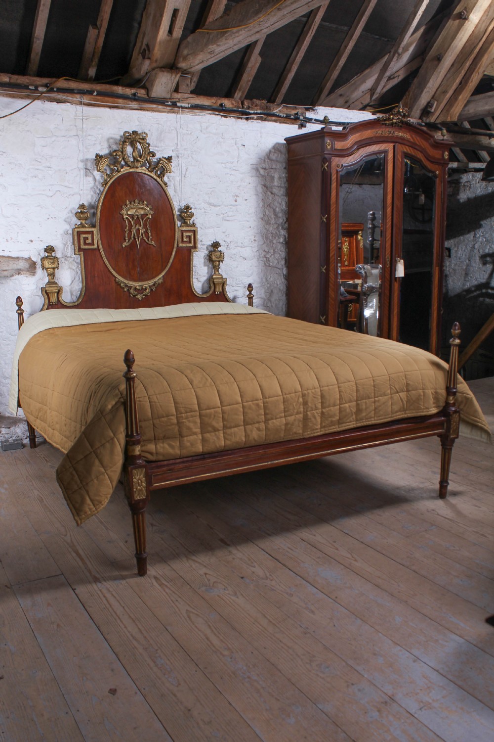 An antique mahogany super king bed featuring a high headboard with an oval central medallion, carved giltwood crest, Greek key motifs, and turned posts. View X
