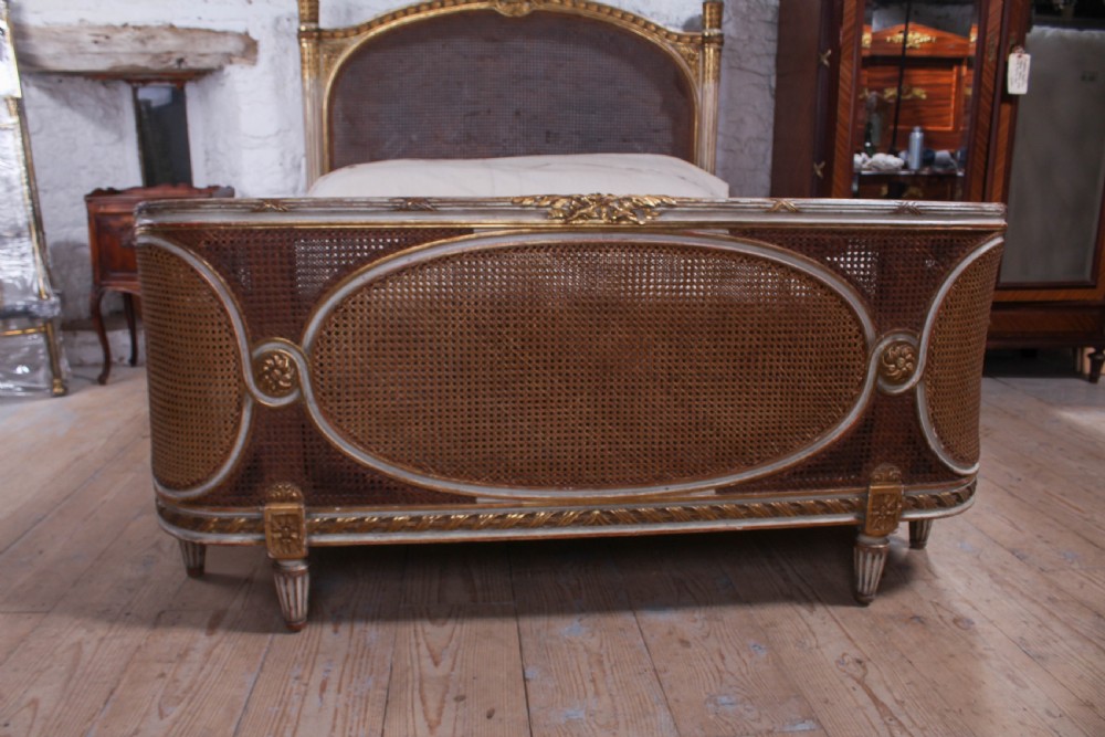 A Louis XVI style French corbeille bed featuring a carved giltwood frame, woven cane panels, fluted legs, and a rounded footboard. View V