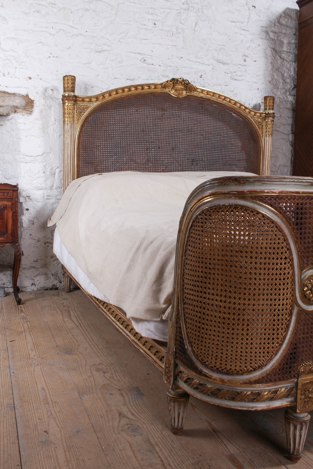 A Louis XVI style French corbeille bed featuring a carved giltwood frame, woven cane panels, fluted legs, and a rounded footboard. View VI