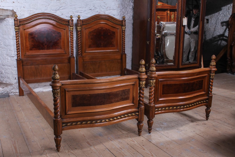 A pair of matching continental mahogany single beds featuring arched headboards, flame veneer panels, spiral turned posts, and gilt pineapple finials.