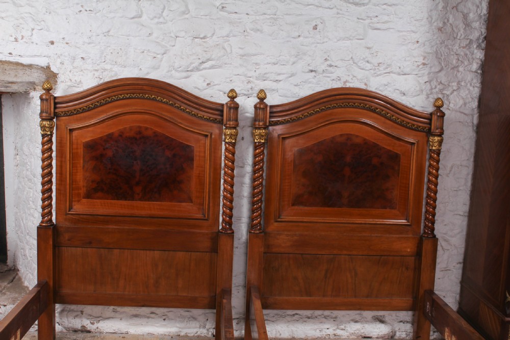 A pair of matching continental mahogany single beds featuring arched headboards, flame veneer panels, spiral turned posts, and gilt pineapple finials. View II