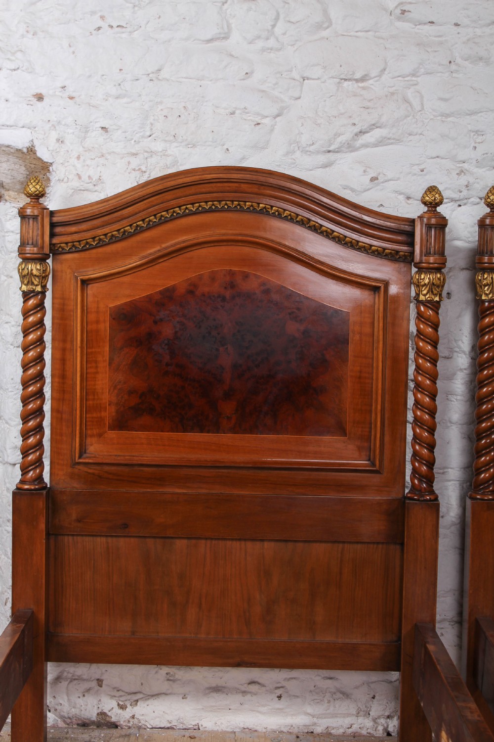A pair of matching continental mahogany single beds featuring arched headboards, flame veneer panels, spiral turned posts, and gilt pineapple finials. View IV