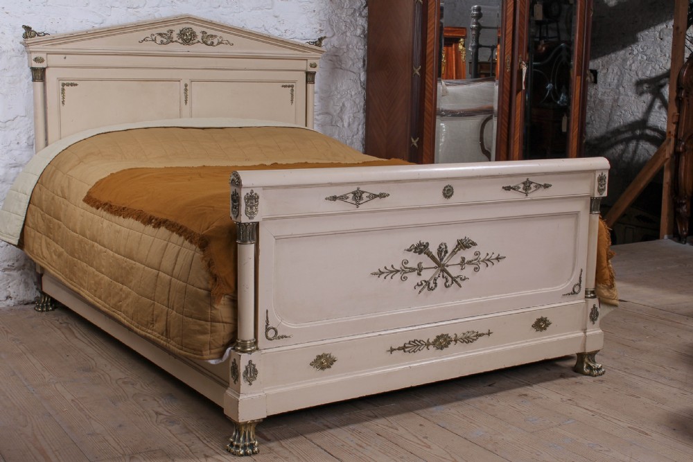 An off-white painted French king-size bedstead featuring gilt metal mounts, torch motifs, and carved claw feet.