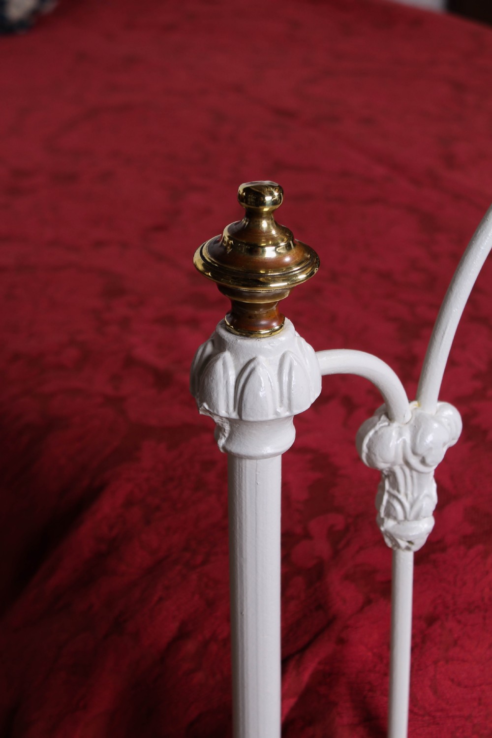 A Victorian white painted wrought iron single bed frame featuring ornate scrollwork, floral metal castings, turned brass finials, and castors. View II