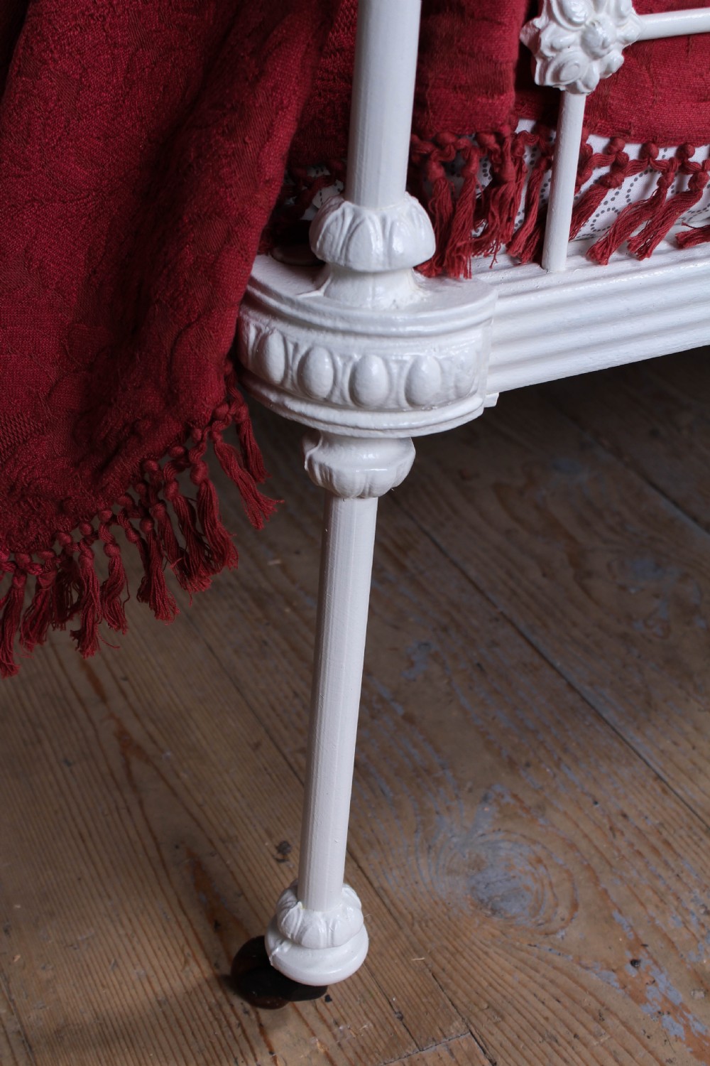 A Victorian white painted wrought iron single bed frame featuring ornate scrollwork, floral metal castings, turned brass finials, and castors. View III
