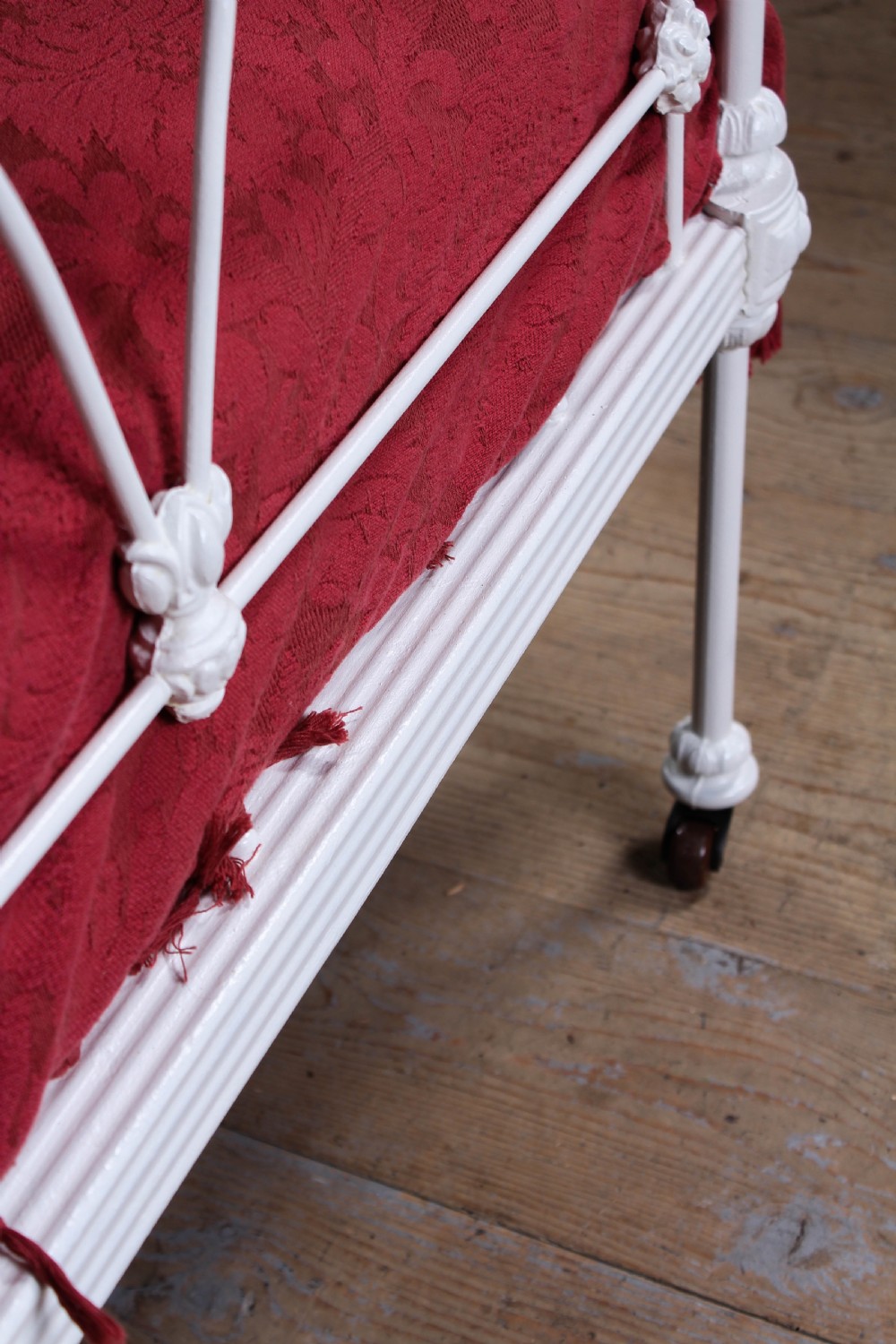 A Victorian white painted wrought iron single bed frame featuring ornate scrollwork, floral metal castings, turned brass finials, and castors. View VII