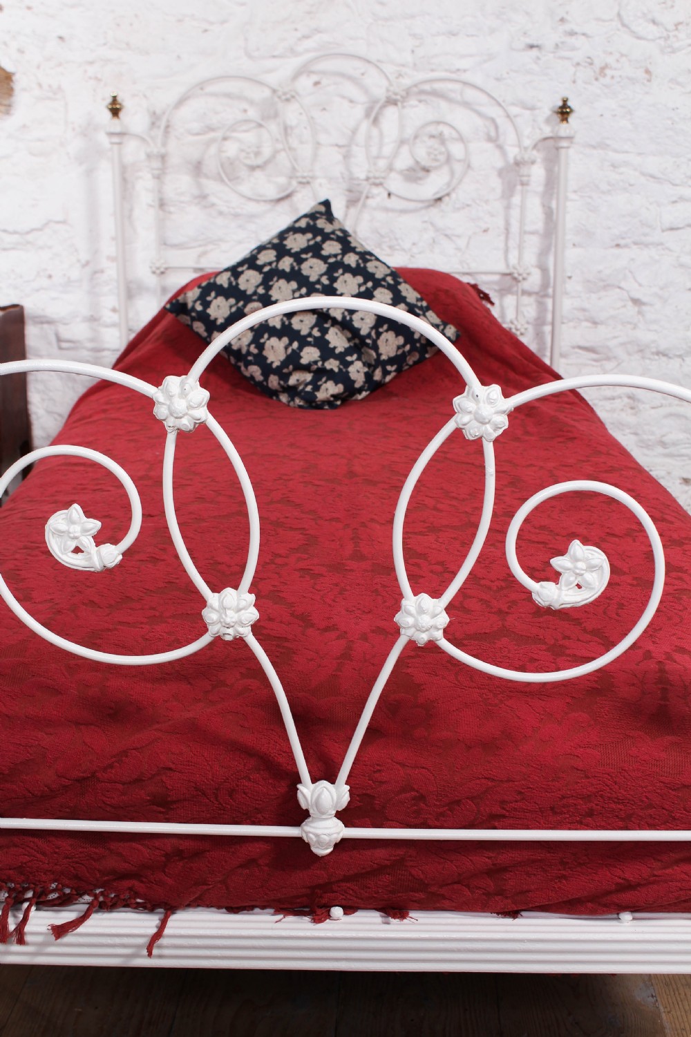 A Victorian white painted wrought iron single bed frame featuring ornate scrollwork, floral metal castings, turned brass finials, and castors. View VIII
