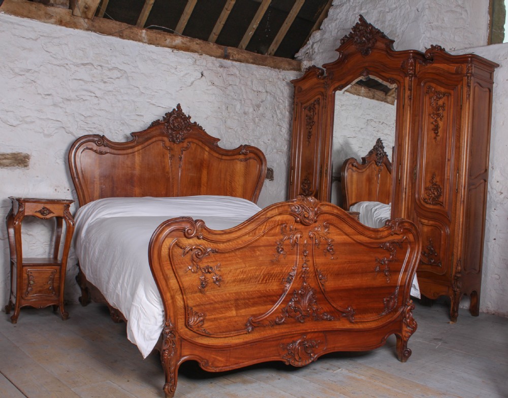 A French Louis XV style carved timber bedroom suite featuring a king-size bedstead, matching bedside cabinet, and three-door mirrored armoire.