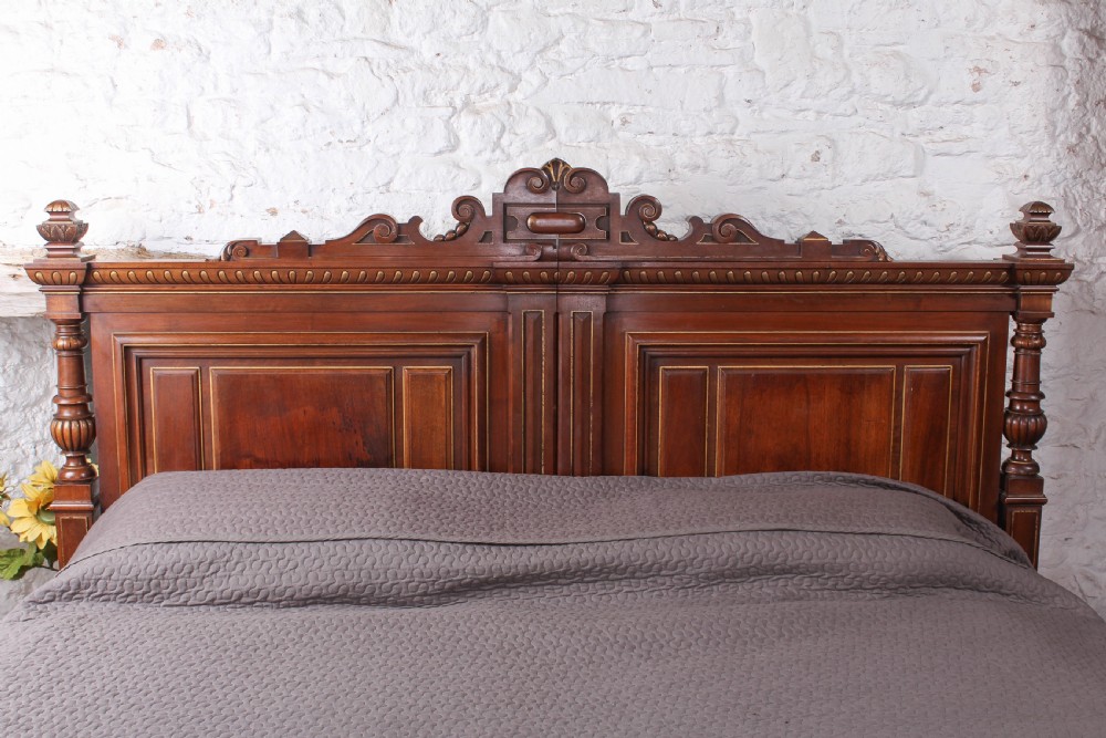 A carved solid walnut emperor size bedstead featuring a cresting motif, geometric panelled headboard and footboard, and turned posts. View II