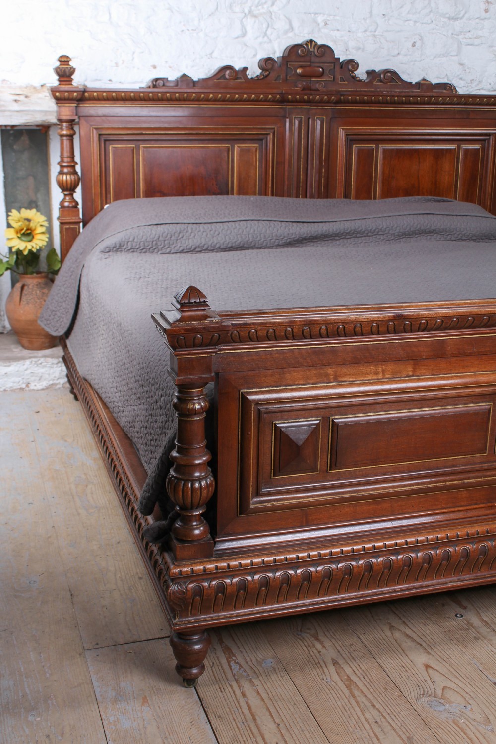 A carved solid walnut emperor size bedstead featuring a cresting motif, geometric panelled headboard and footboard, and turned posts. View IV