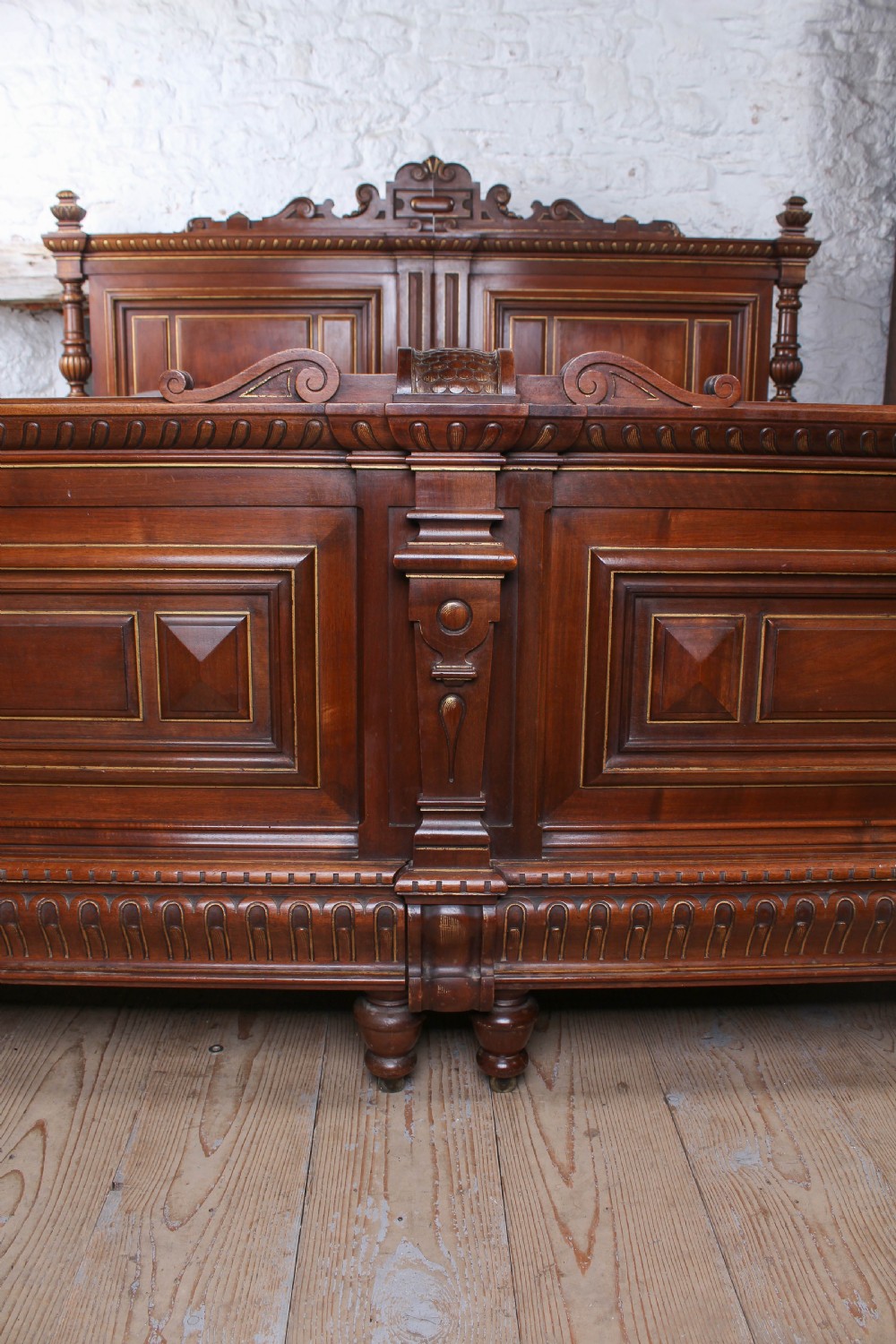 A carved solid walnut emperor size bedstead featuring a cresting motif, geometric panelled headboard and footboard, and turned posts. View V