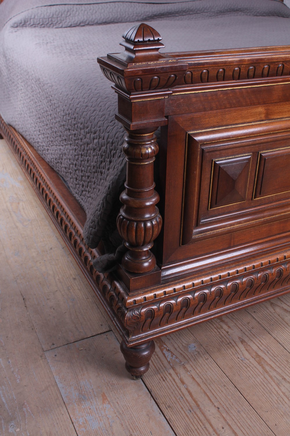 A carved solid walnut emperor size bedstead featuring a cresting motif, geometric panelled headboard and footboard, and turned posts. View VI