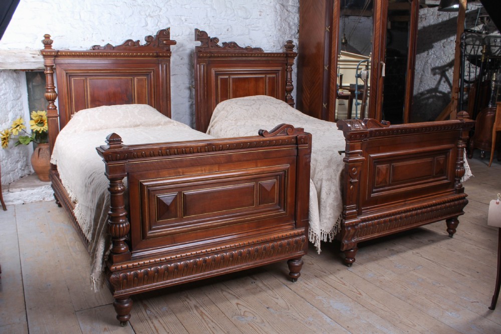A carved solid walnut emperor size bedstead featuring a cresting motif, geometric panelled headboard and footboard, and turned posts. View VIII