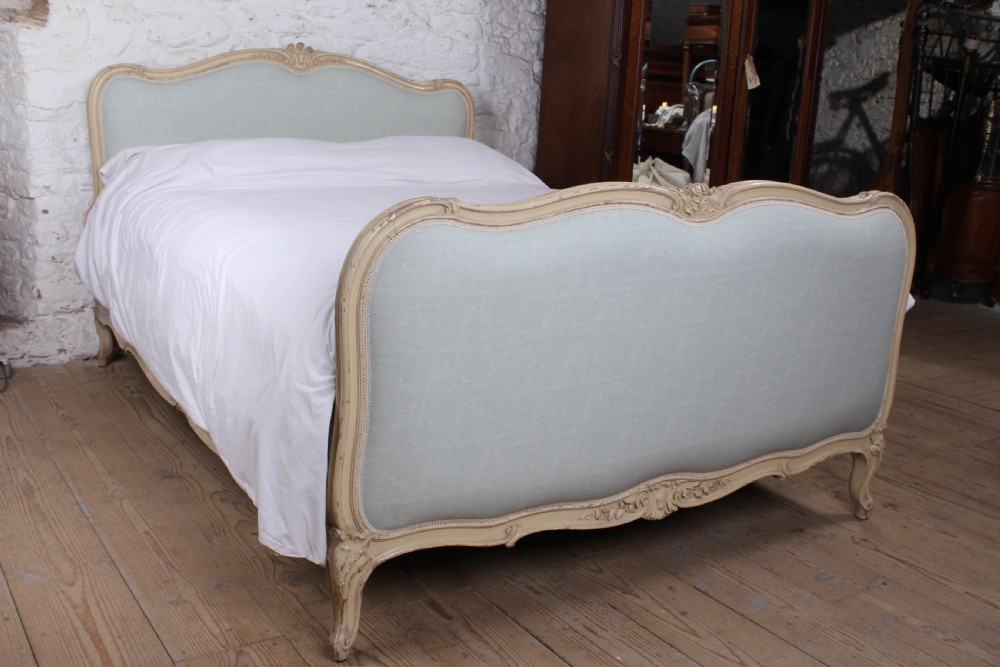 A Louis XV style king-size bed frame featuring a carved cream painted timber surround, upholstered headboard and footboard in pale blue fabric, resting on cabriole legs.