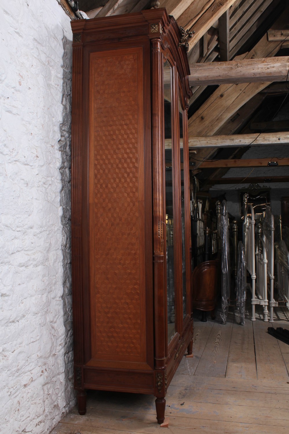 A tall French Louis XVI Revival warm brown wood armoire featuring arched twin mirrored doors, parquetry side panels, and decorative brass mounts. View IV