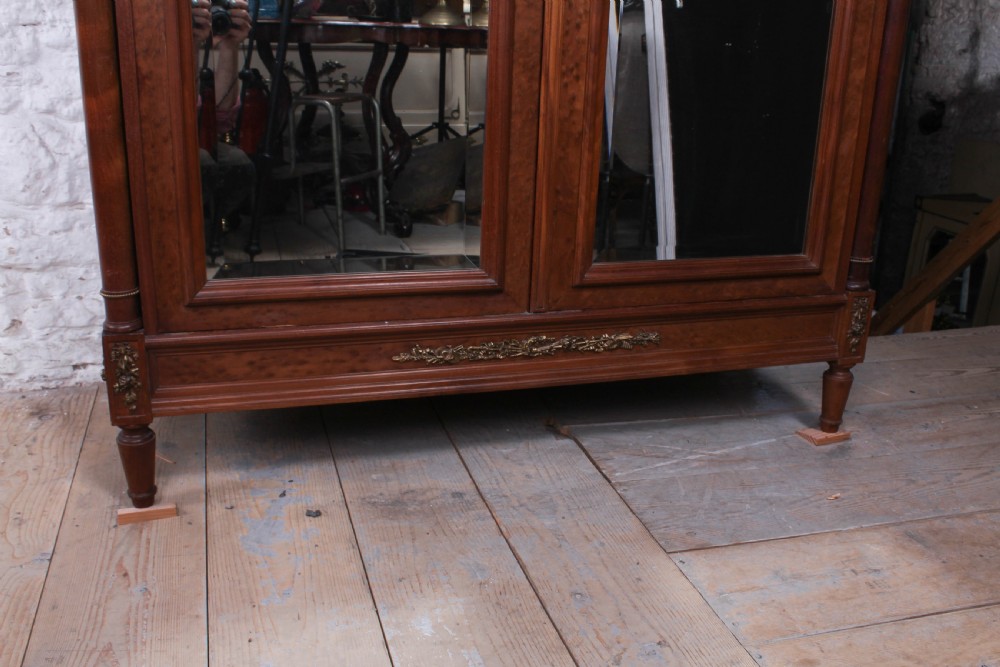 A tall French Louis XVI Revival warm brown wood armoire featuring arched twin mirrored doors, parquetry side panels, and decorative brass mounts. View VII