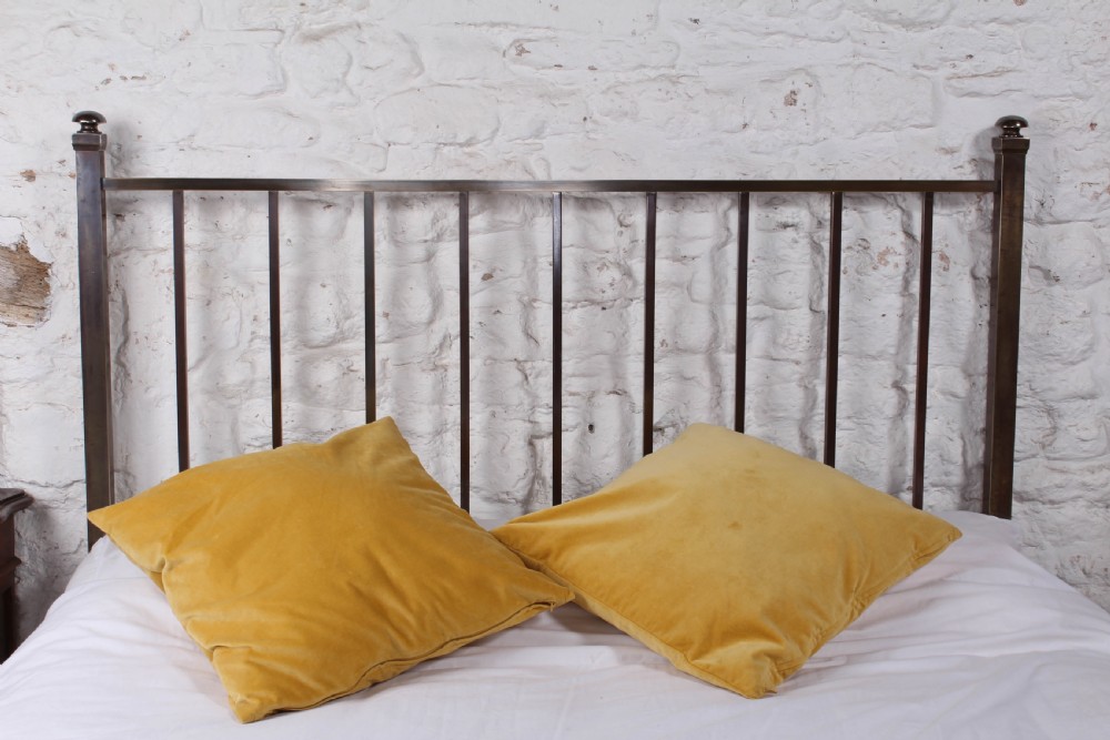 An antique Victorian king-size bed frame featuring vertical brass spindles, square corner posts, and an aged metallic patina set on castors. View V