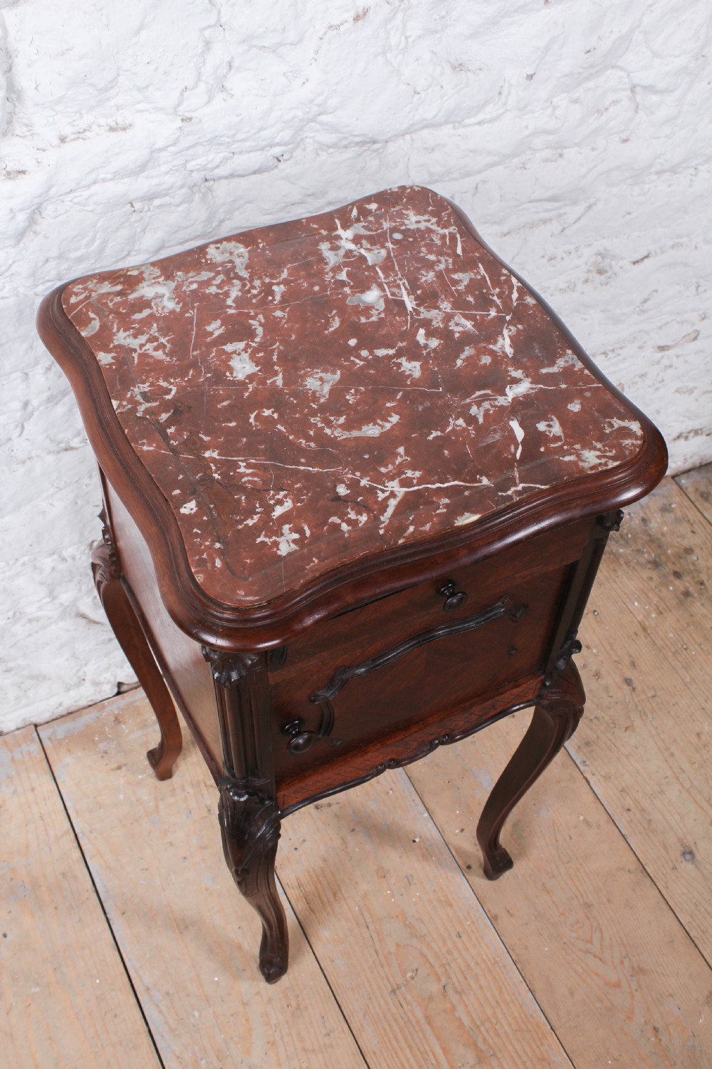 A dark wood Louis XV style bedside cabinet featuring an inset marble top, quarter-veneered door, drawer, carved apron, and tall cabriole legs. View IV