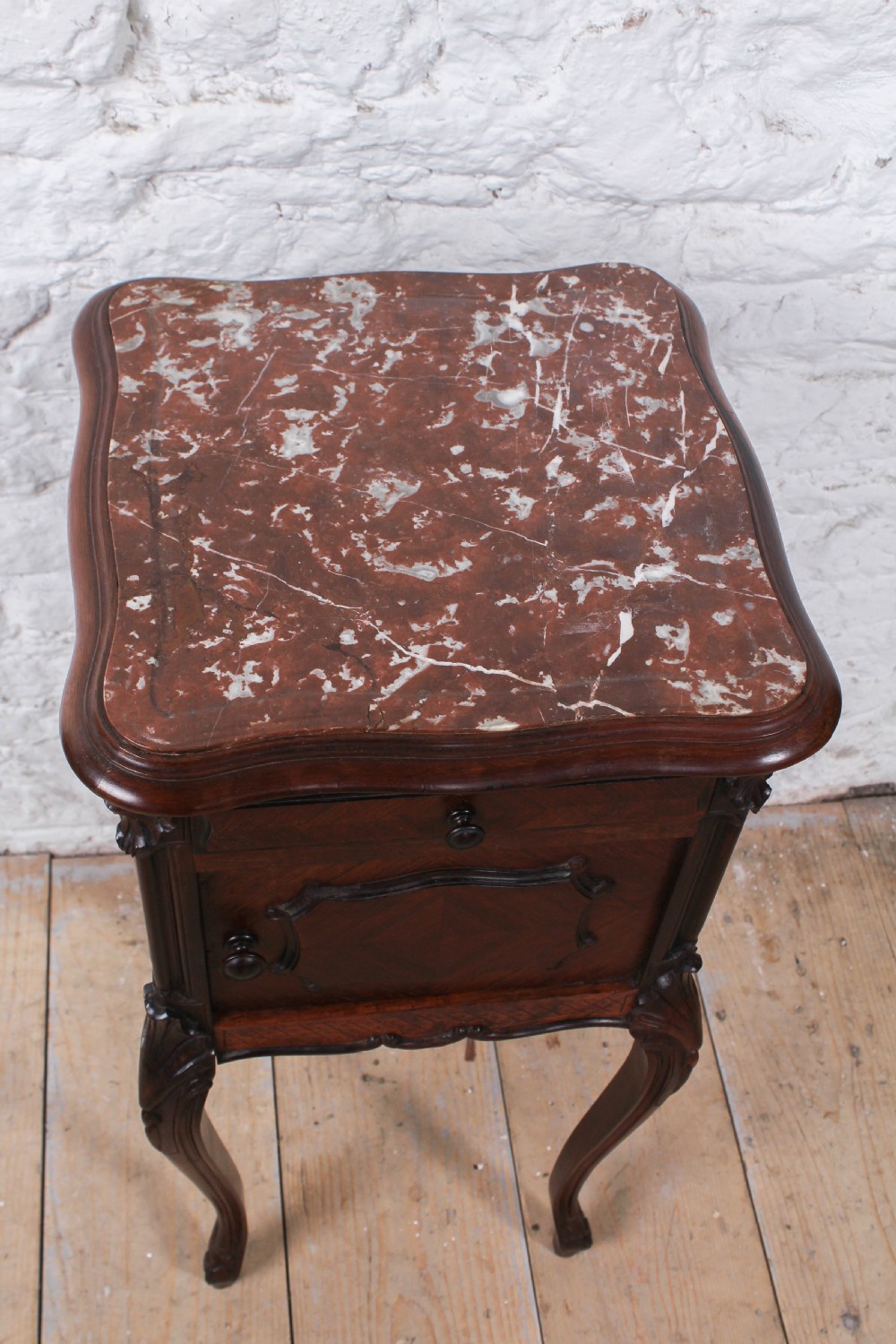 A dark wood Louis XV style bedside cabinet featuring an inset marble top, quarter-veneered door, drawer, carved apron, and tall cabriole legs. View V