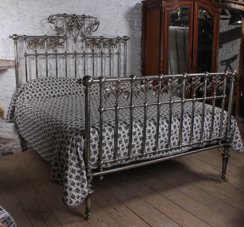 A nickel-plated super king size bedstead featuring Art Nouveau floral metalwork detailing on the arched headboard and footboard.