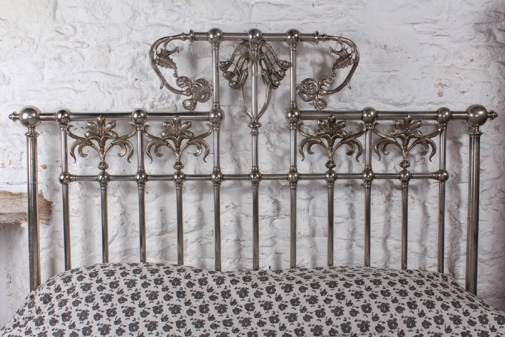 A nickel-plated super king size bedstead featuring Art Nouveau floral metalwork detailing on the arched headboard and footboard. View VII