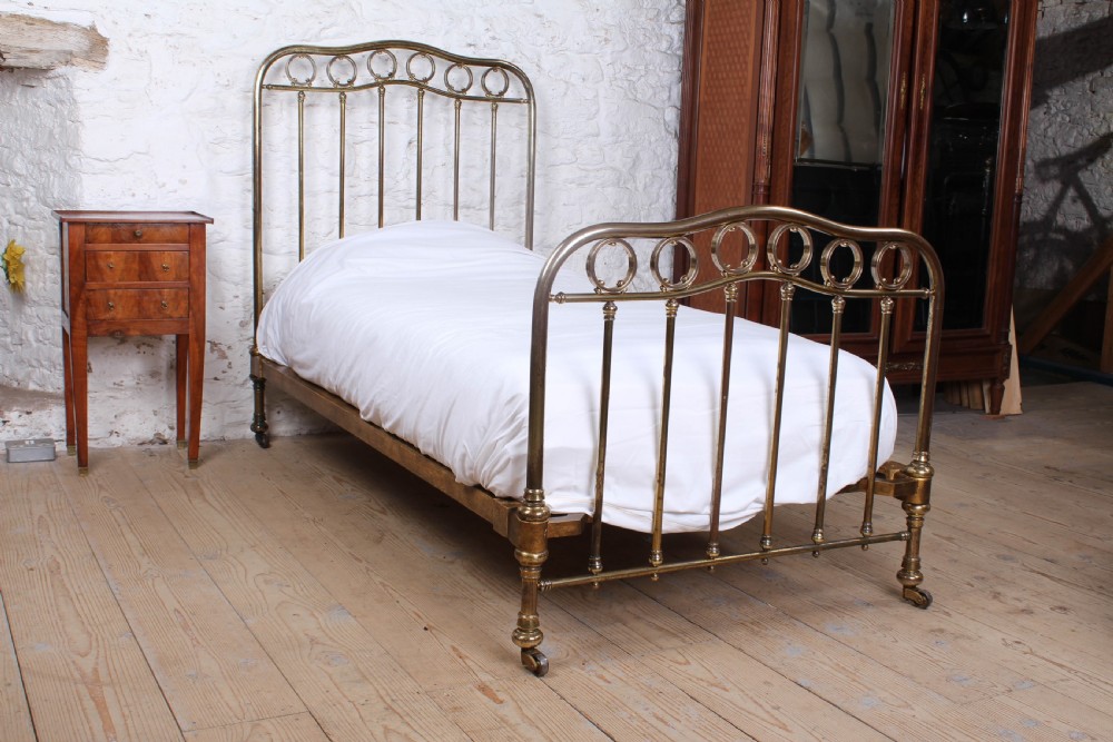 An antique French brass single bed frame featuring an arched headboard and footboard decorated with circular hoop motifs and vertical spindles.