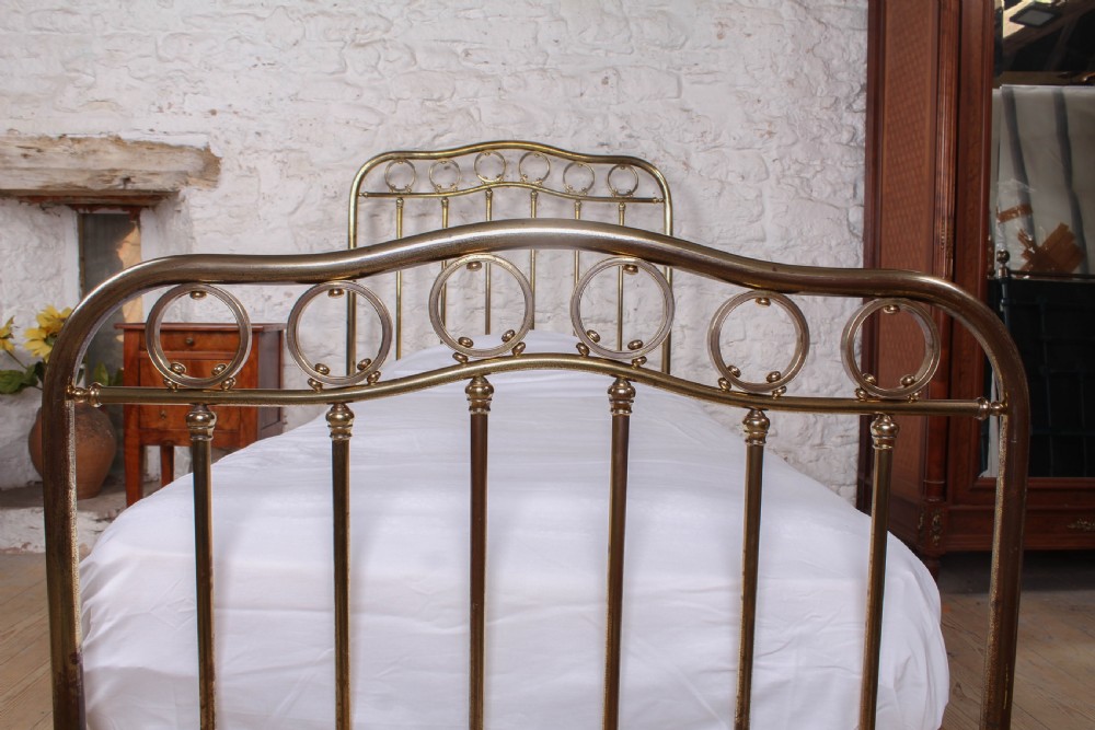 An antique French brass single bed frame featuring an arched headboard and footboard decorated with circular hoop motifs and vertical spindles. View III