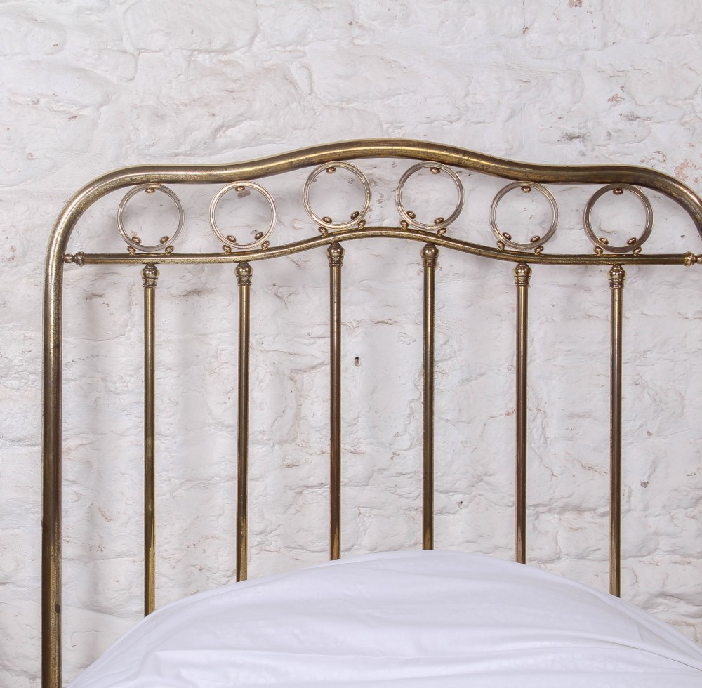 An antique French brass single bed frame featuring an arched headboard and footboard decorated with circular hoop motifs and vertical spindles. View IV