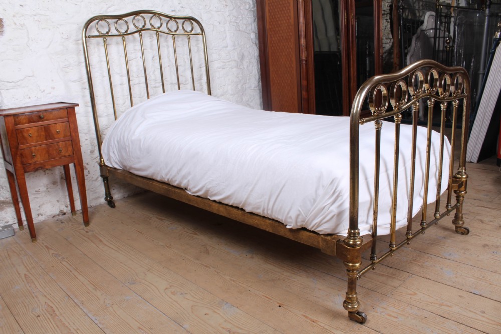 An antique French brass single bed frame featuring an arched headboard and footboard decorated with circular hoop motifs and vertical spindles. View VI