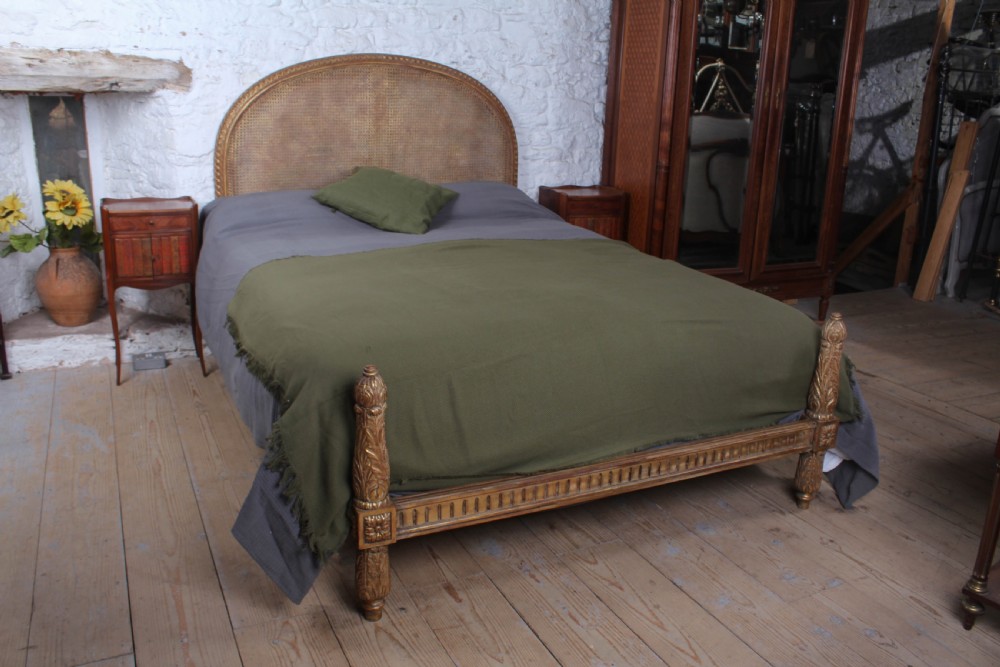 A French Neoclassical king-size bed featuring a carved giltwood frame with an arched caned headboard and detailed fluted posts.