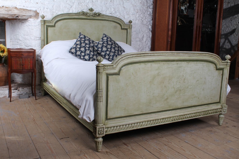 A French Louis XVI style king size bedstead in distressed sage green paint with carved fluted posts and decorative molding.