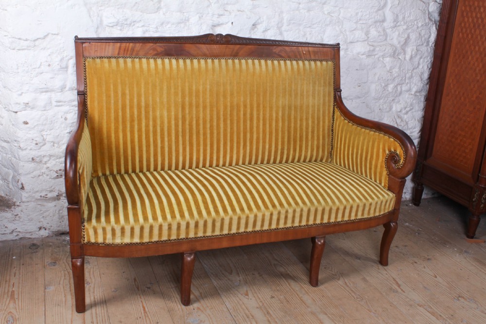 A French Directoire two-seater sofa featuring a polished fruitwood frame and yellow striped velvet upholstery secured with brass studding.