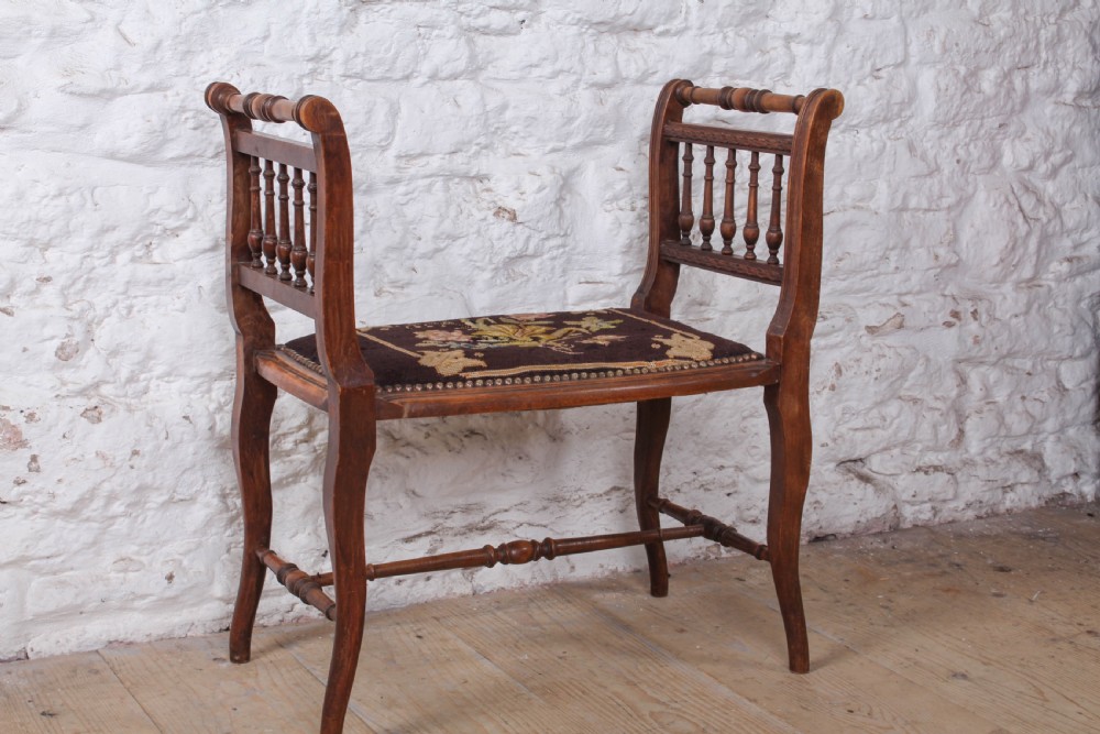 A French wooden stool featuring raised spindled side galleries, turned stretchers, and a dark floral tapestry seat fastened with brass studs.