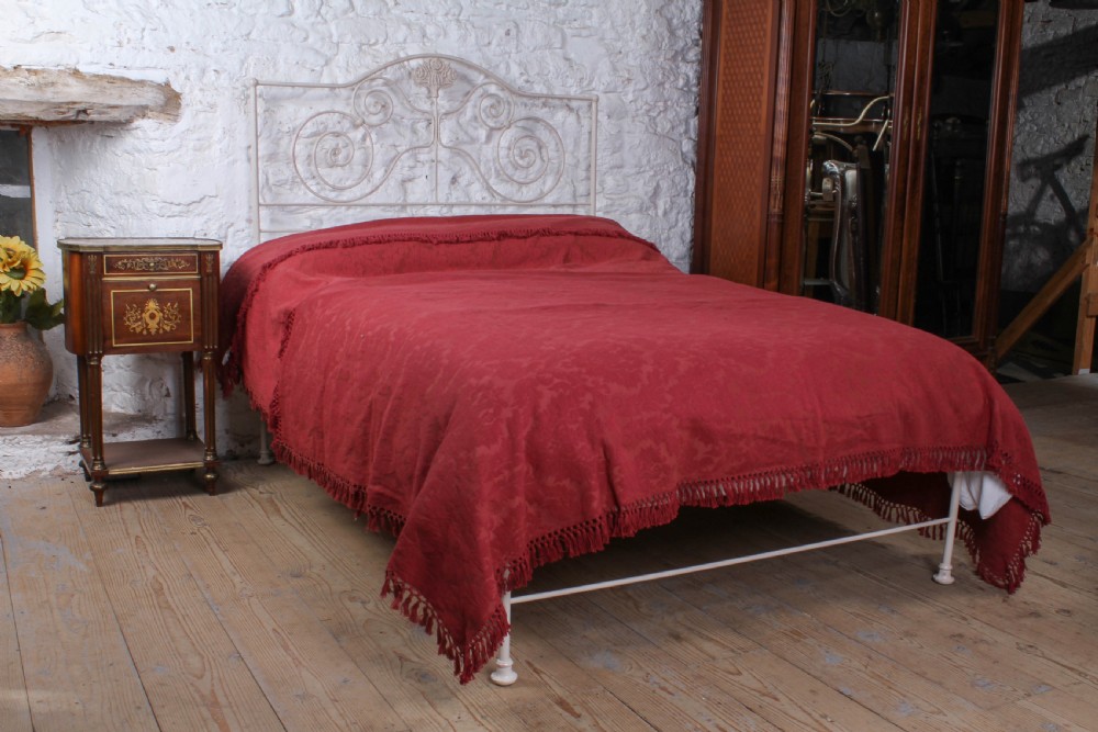 An off-white painted forged iron double bed frame featuring an arched headboard decorated with scrollwork and a low-profile foot end.