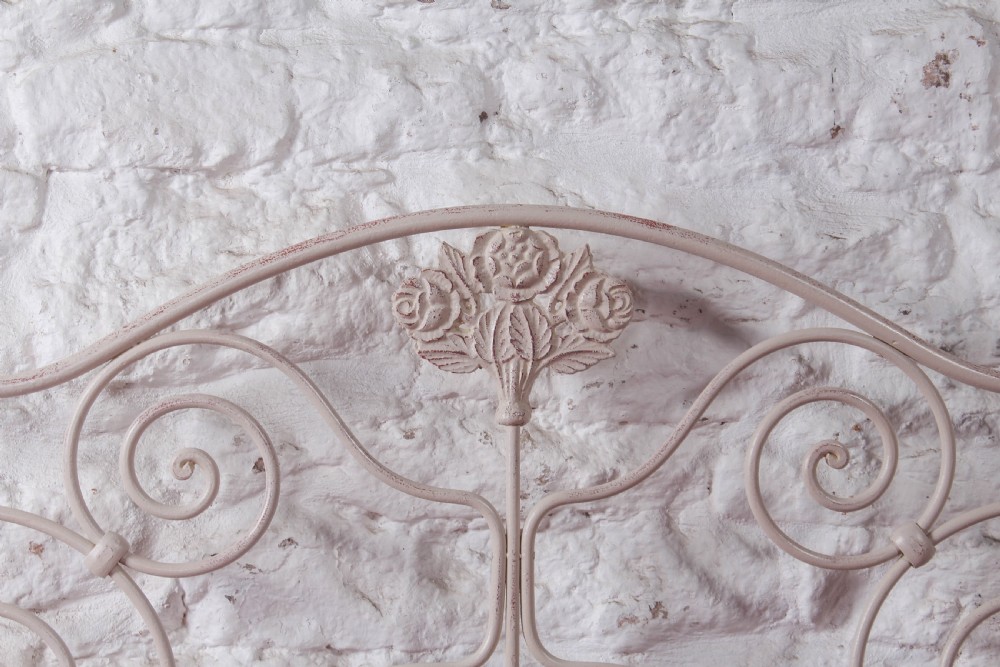 An off-white painted forged iron double bed frame featuring an arched headboard decorated with scrollwork and a low-profile foot end. View VI