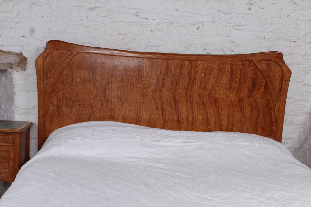 An Art Nouveau wooden bedroom suite featuring a curved double bedstead, matching dressing table with mirror, nightstand, and leather-upholstered side chairs. View III