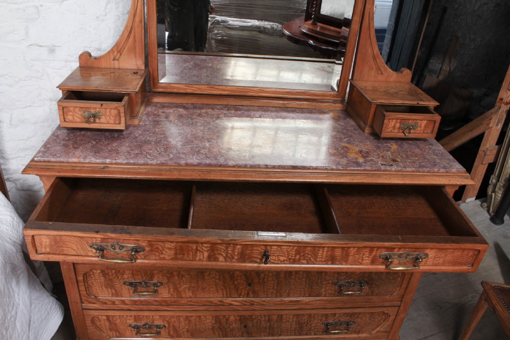 An Art Nouveau wooden bedroom suite featuring a curved double bedstead, matching dressing table with mirror, nightstand, and leather-upholstered side chairs. View XIV