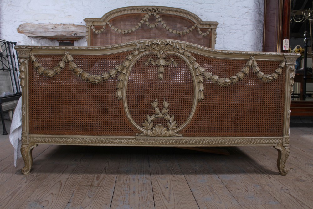 A French Louis XVI style super king bedstead featuring woven rattan cane panels, carved floral swags, and matching caned side chairs in a painted distressed finish. View II