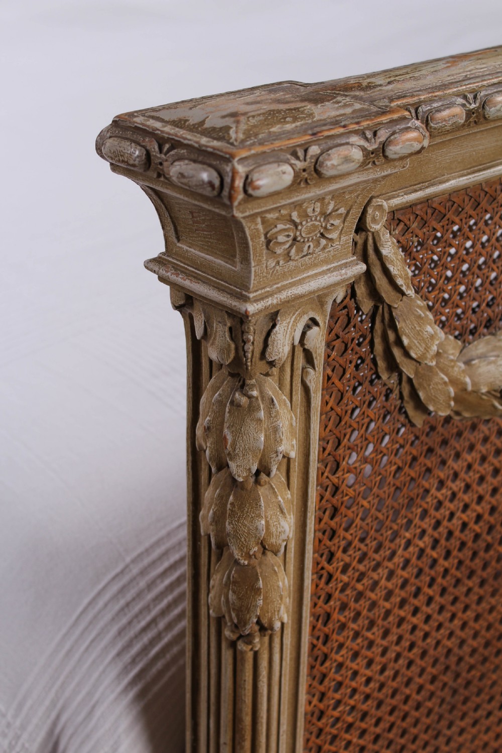 A French Louis XVI style super king bedstead featuring woven rattan cane panels, carved floral swags, and matching caned side chairs in a painted distressed finish. View IV