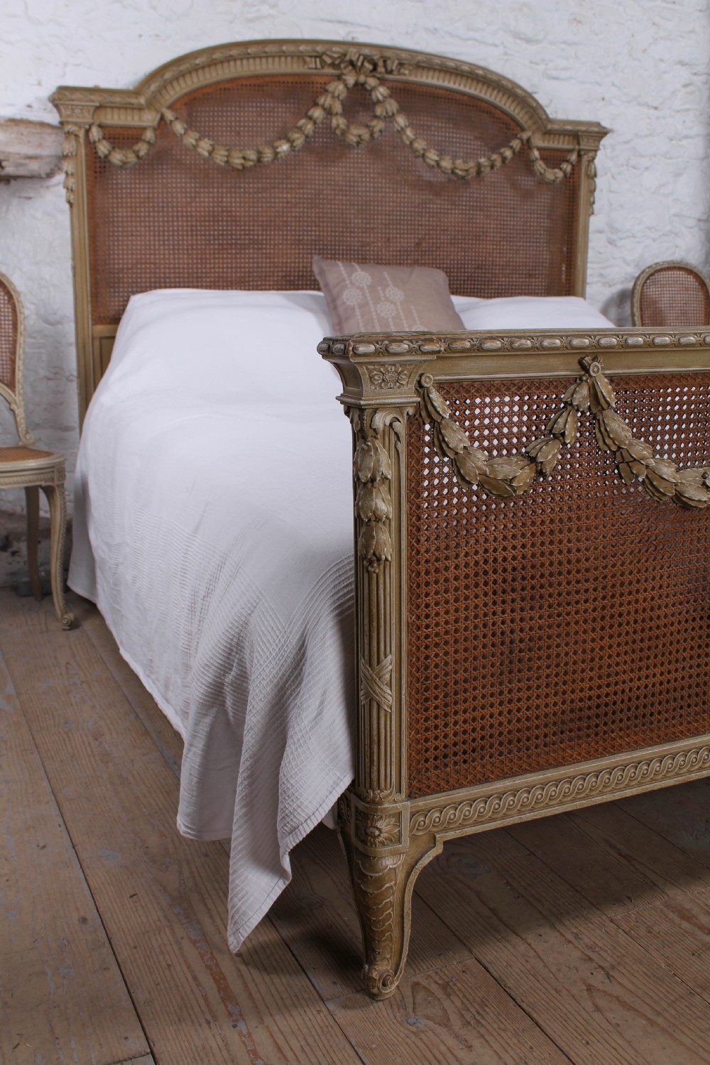 A French Louis XVI style super king bedstead featuring woven rattan cane panels, carved floral swags, and matching caned side chairs in a painted distressed finish. View V