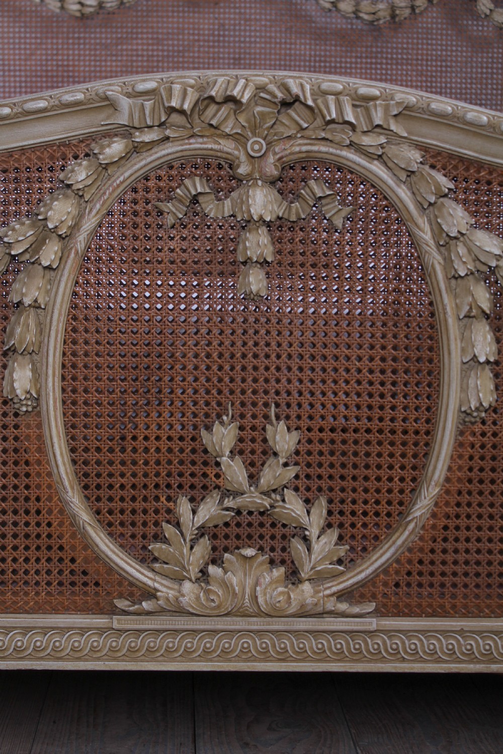 A French Louis XVI style super king bedstead featuring woven rattan cane panels, carved floral swags, and matching caned side chairs in a painted distressed finish. View VII