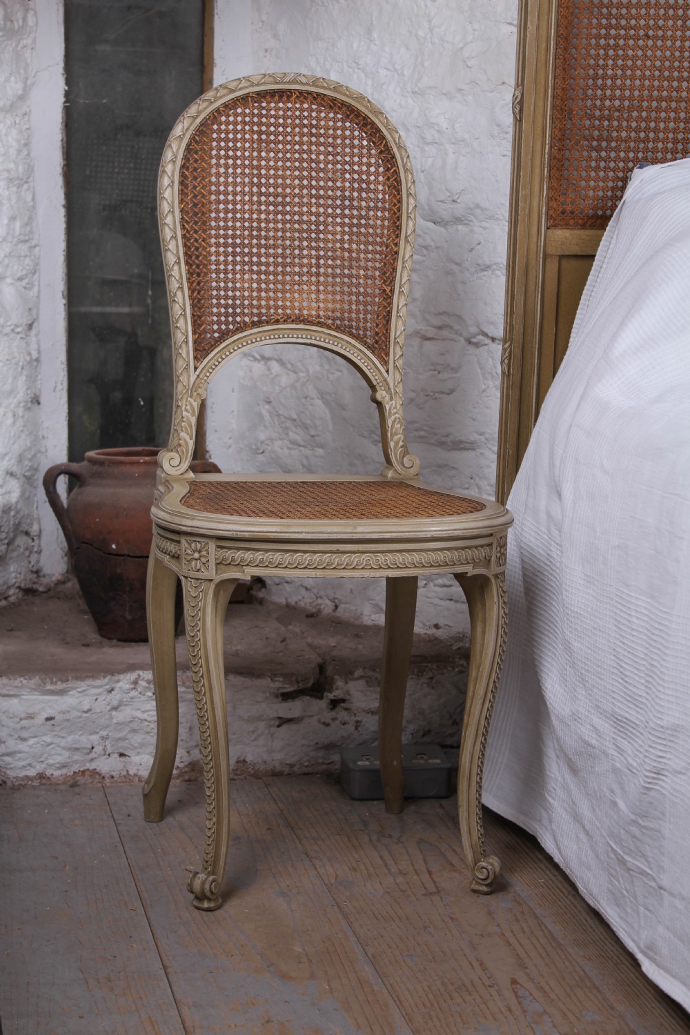 A French Louis XVI style super king bedstead featuring woven rattan cane panels, carved floral swags, and matching caned side chairs in a painted distressed finish. View VIII